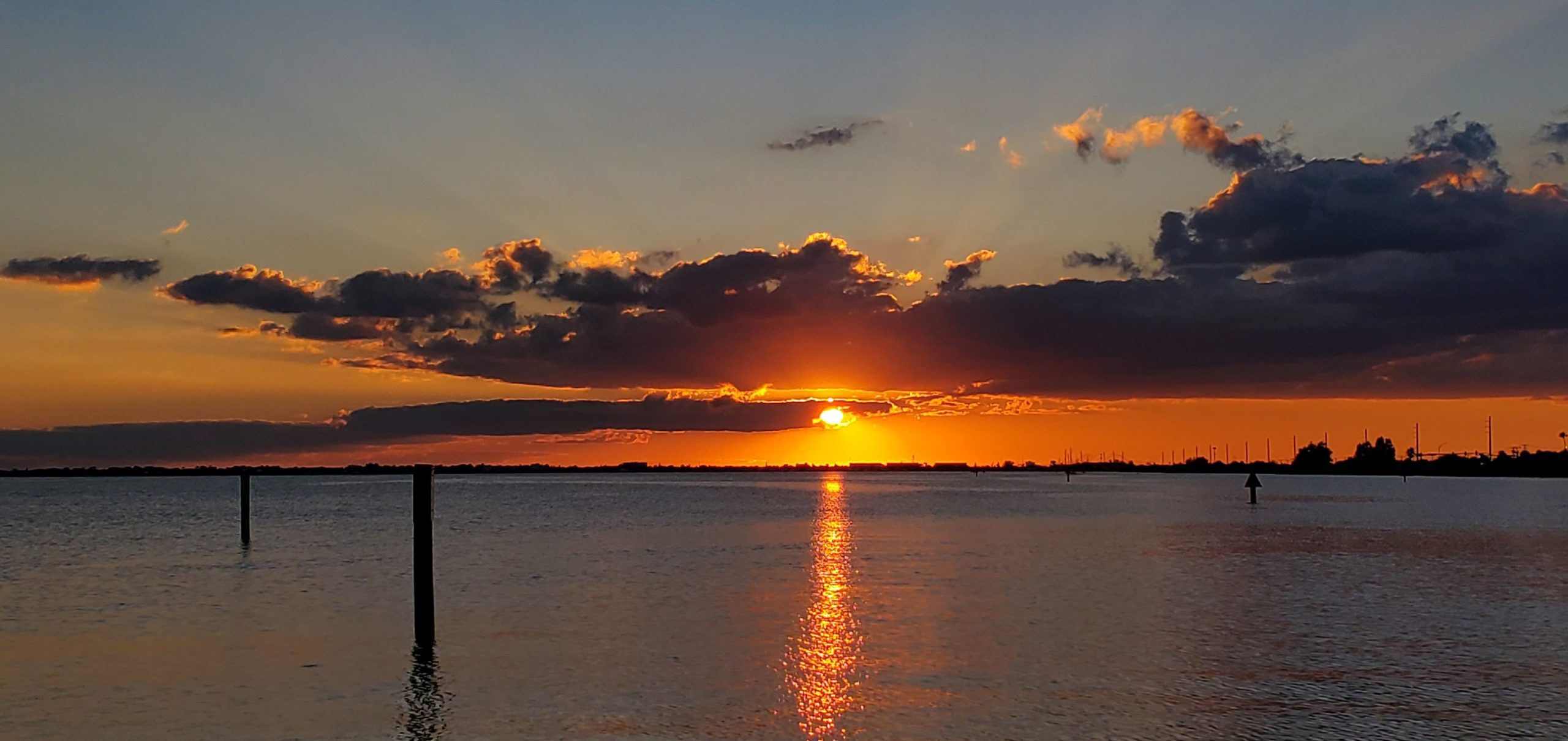 Orange sunset reflecting on the water with silhouetted palm trees on the shoreline