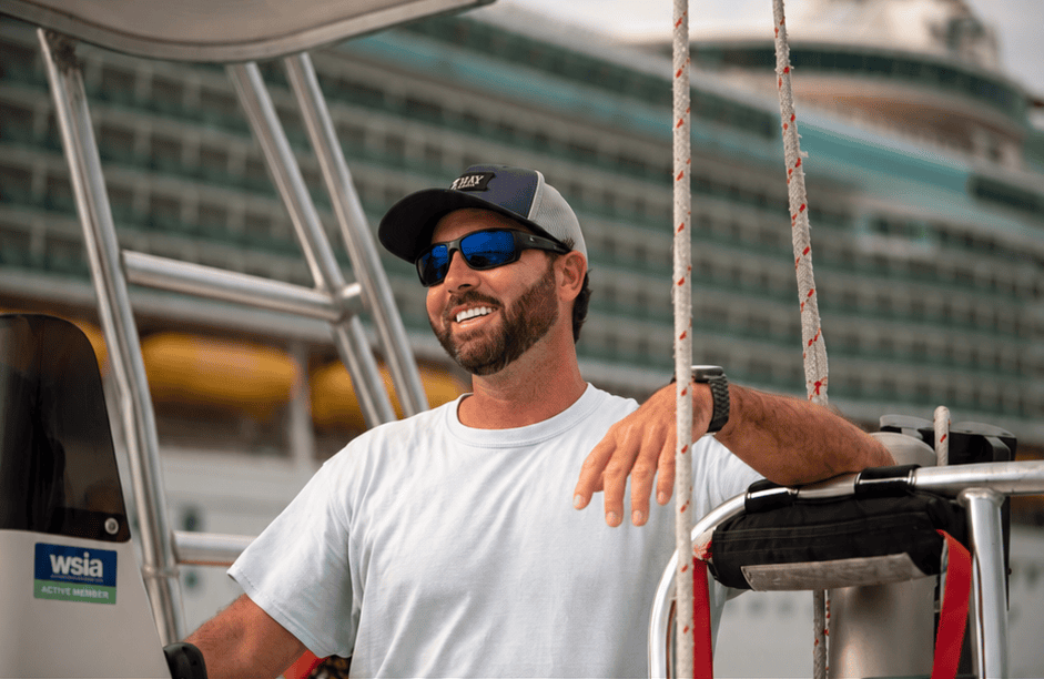 Captain Angus Johnson smiling aboard his boat with a cruise ship behind him in Port Canaveral